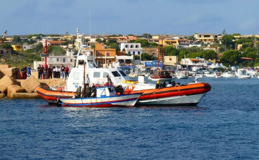 la guardia costiera di lampedusa accanto a un barchino di migranti (ansa)